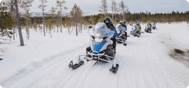 A group of people riding snowmobiles on a snowy road