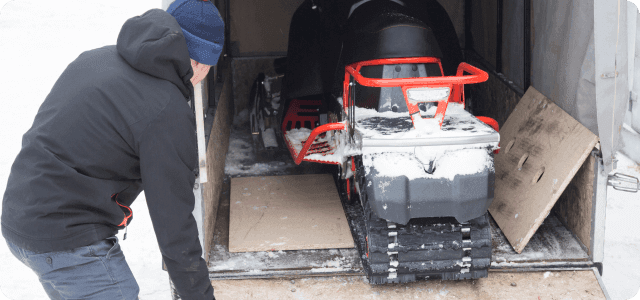 A man taking a snowmobile out of a trailer