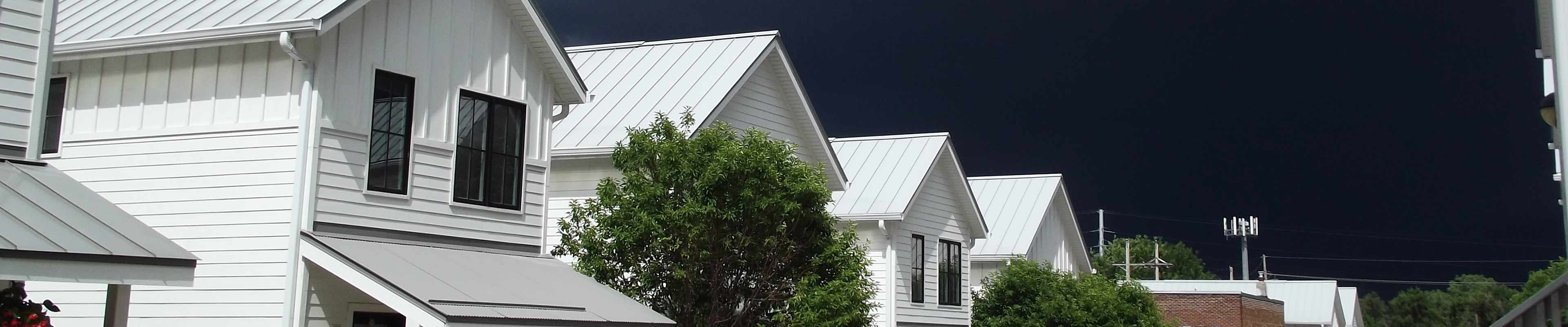 A row of houses in a neighborhood with storm clouds that will bring strong rain and roof leaks behind it.